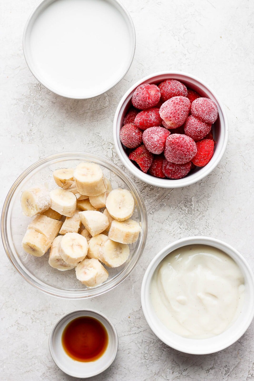 Strawberry banana smoothie ingredients in small bowls.