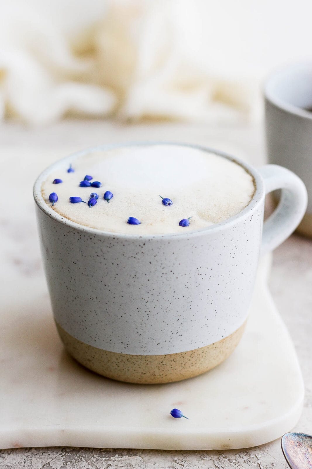 A mug of a London Fog on a marble slab with purple flower petals as garnish. 