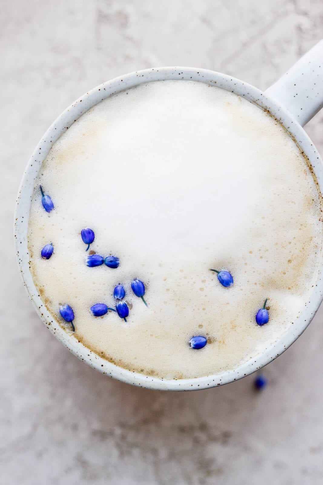 A mug of a London Fog on a marble slab with purple flower petals as garnish. 