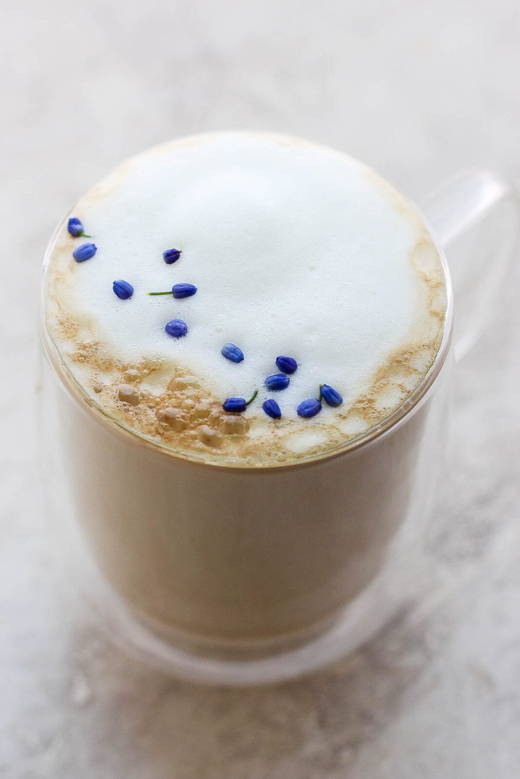 A mug of a London Fog on a marble slab with purple flower petals as garnish. 