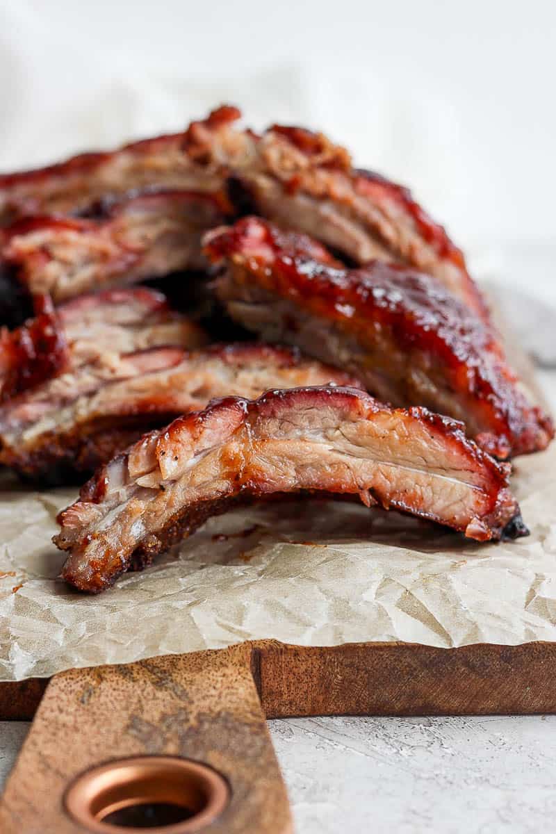 A pile of ribs sitting on a wooden board and a piece of parchment paper. 