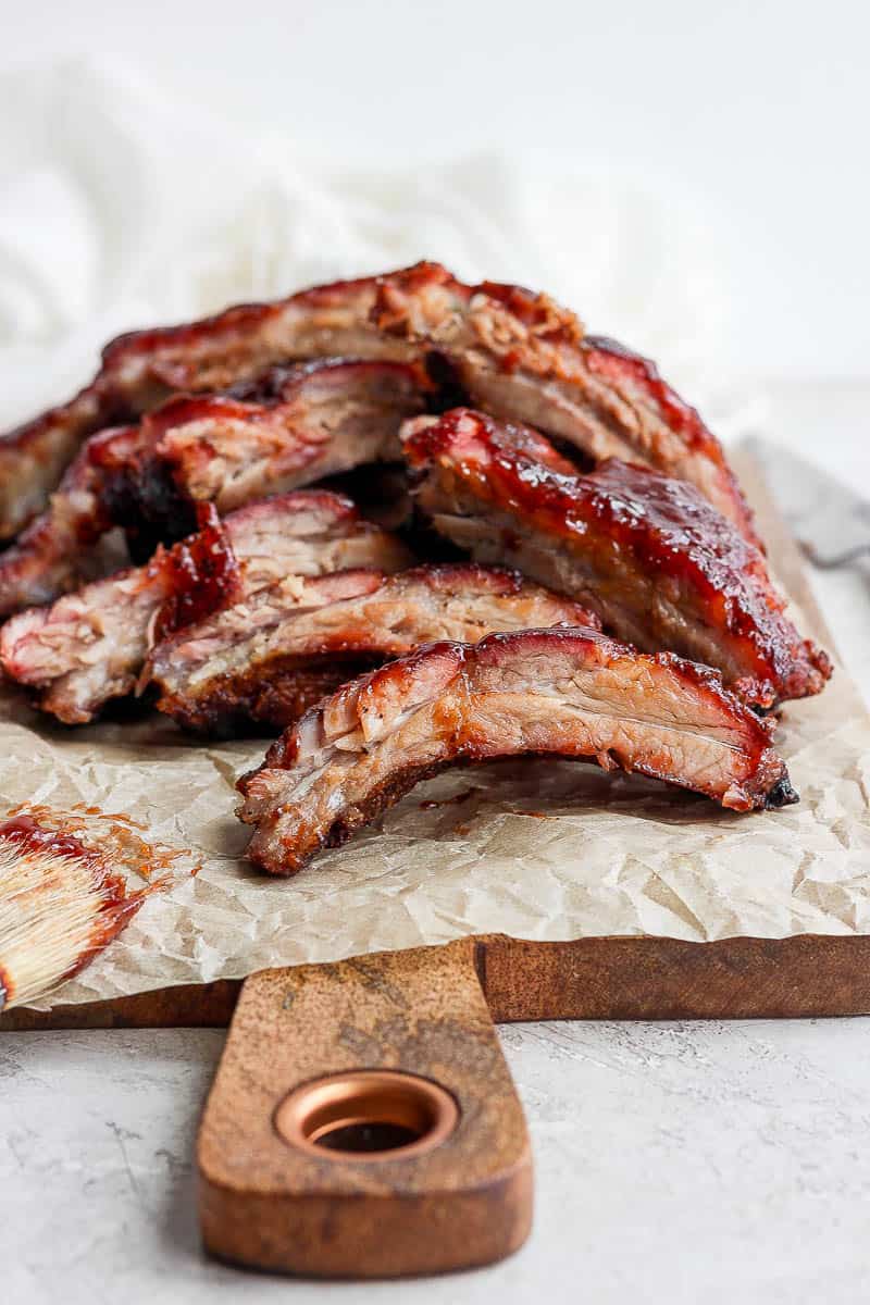 Oven baked ribs sitting on a wooden board and piece of parchment paper. 