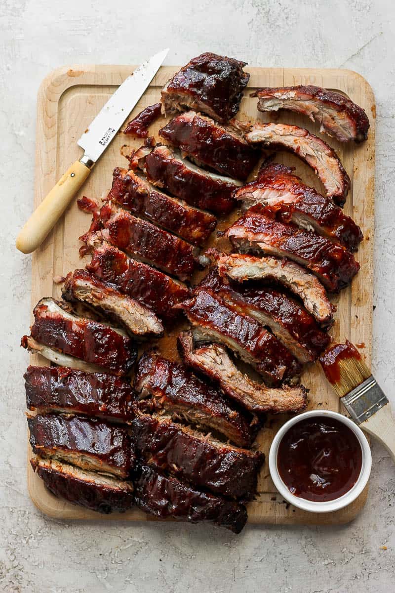 A wooden cutting board with two racks of ribs on top, but into slices. 