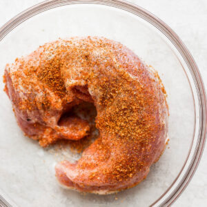 A large glass bowl with a pork tenderloin covered in the pork tenderloin dry rub.