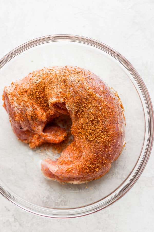 A large glass bowl with a pork tenderloin covered in the pork tenderloin dry rub.