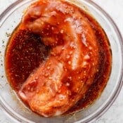 A large glass bowl with a pork tenderloin and the tenderloin marinade.