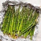 A large piece of aluminum foil with several stalks of smoked asparagus.