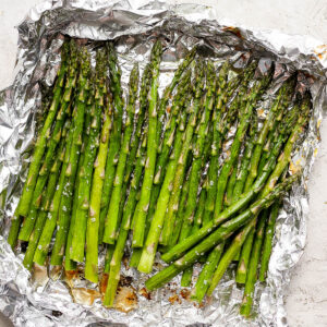 A large piece of aluminum foil with several stalks of smoked asparagus.