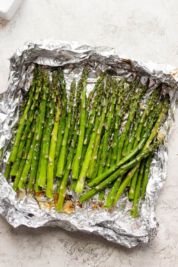 A large piece of aluminum foil with several stalks of smoked asparagus.