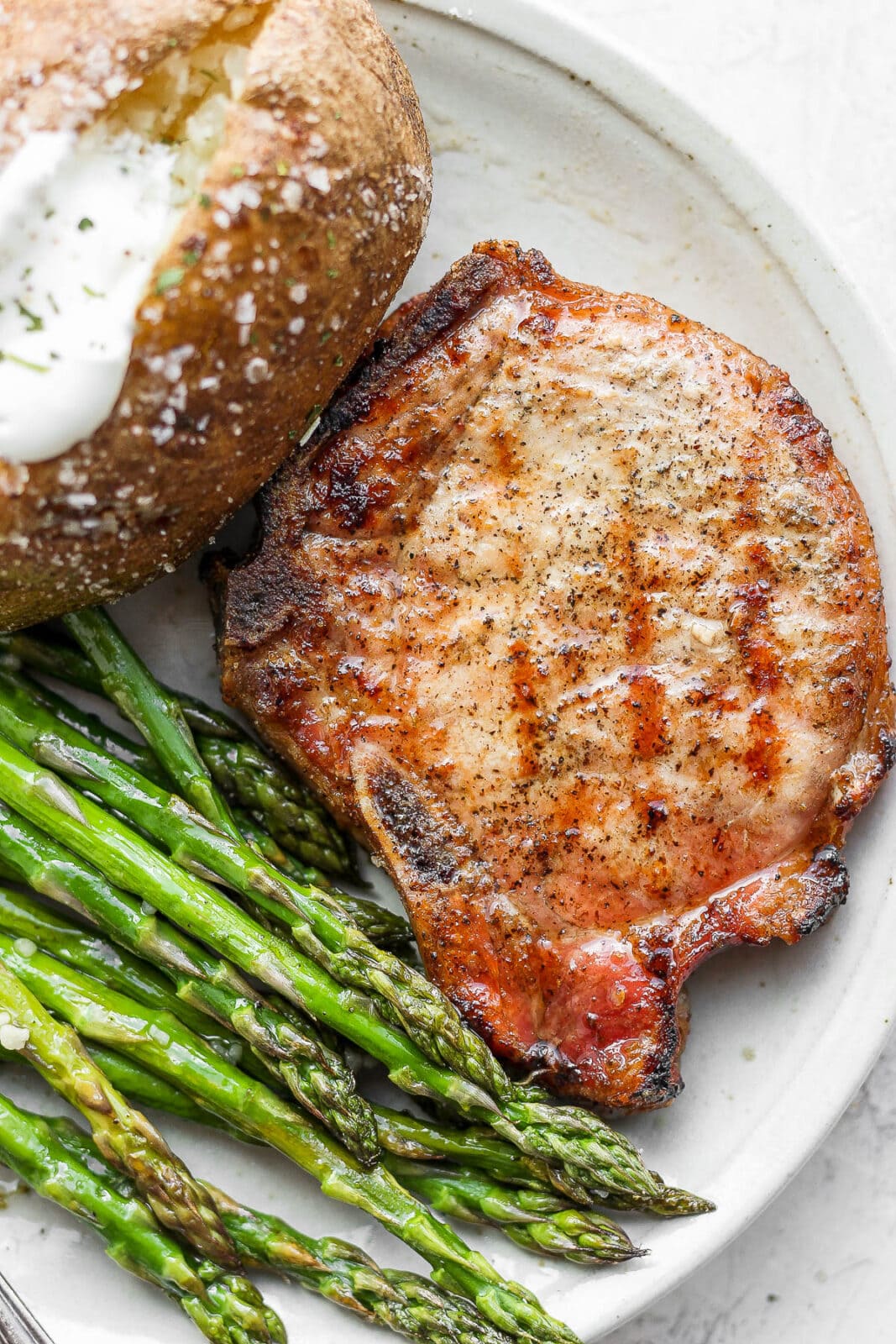 A plate with smoked asparagus, a pork chop, and a baked potato.