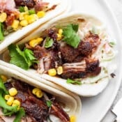 A white plate with three smoked carnitas tacos next to each other.