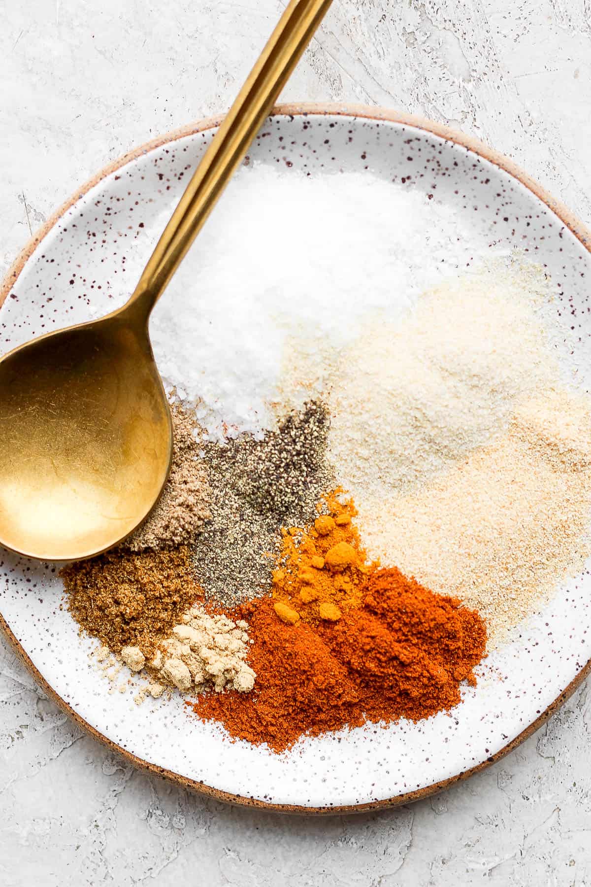 A plate with dry rub ingredients on it and a golden spoon. 