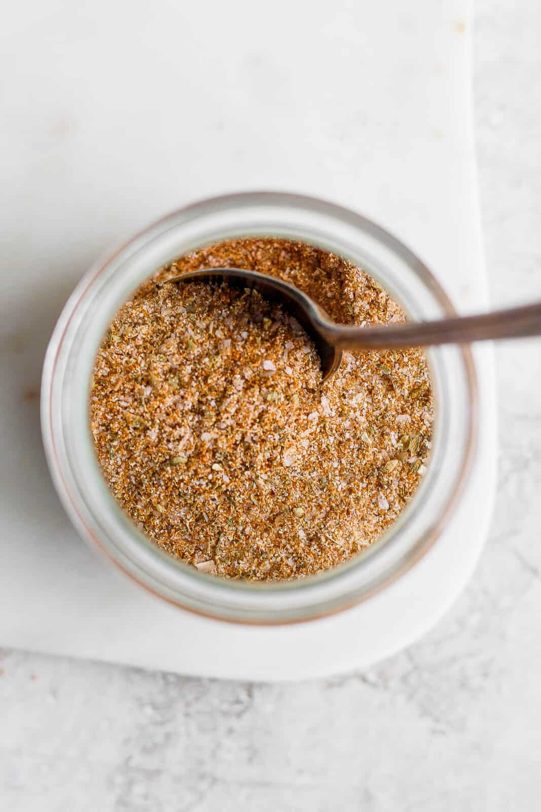 A glass filled with dry rub and a spoon sticking out of it. 