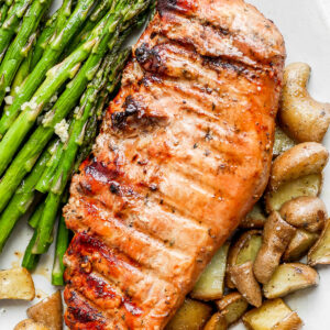 A large plate with a smoked pork tenderloin, potatoes, and asparagus.