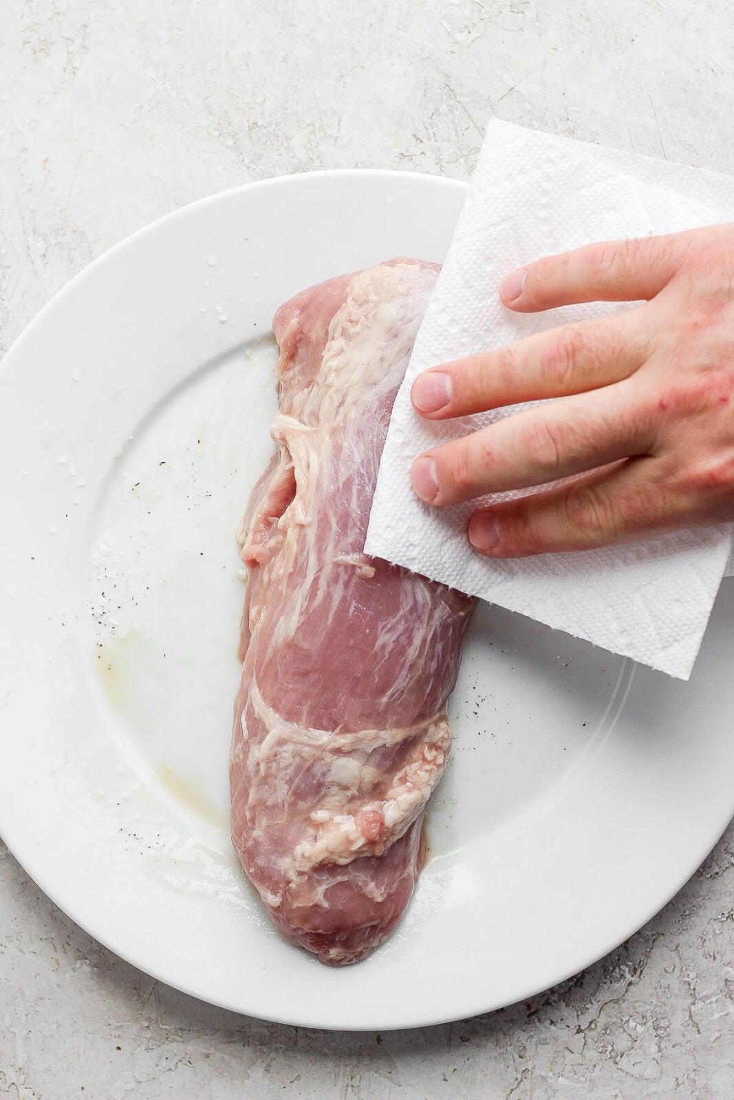 Someone patting dry a raw pork tenderloin with a clean paper towel. 