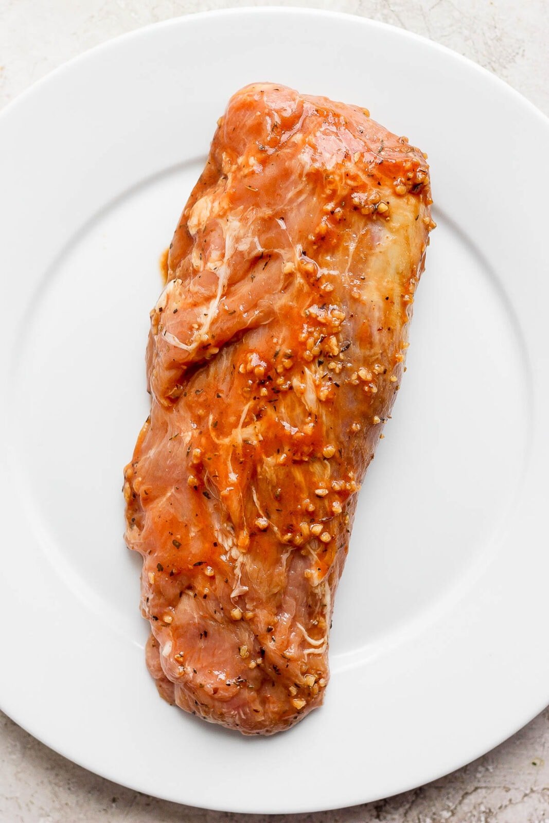 A pork tenderloin on a plate covered in marinade. 