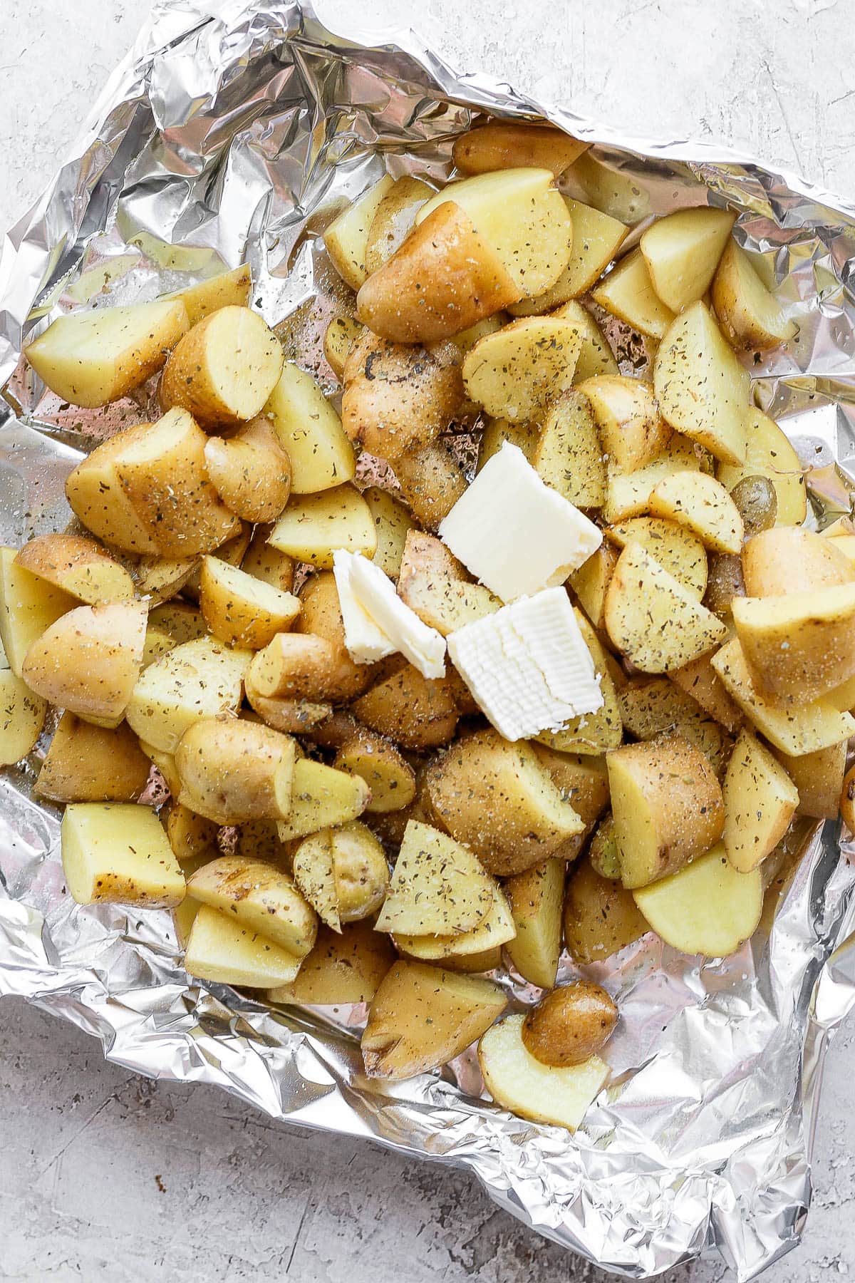 Seasoned potatoes in an aluminum foil boat with a dollop of butter on top.