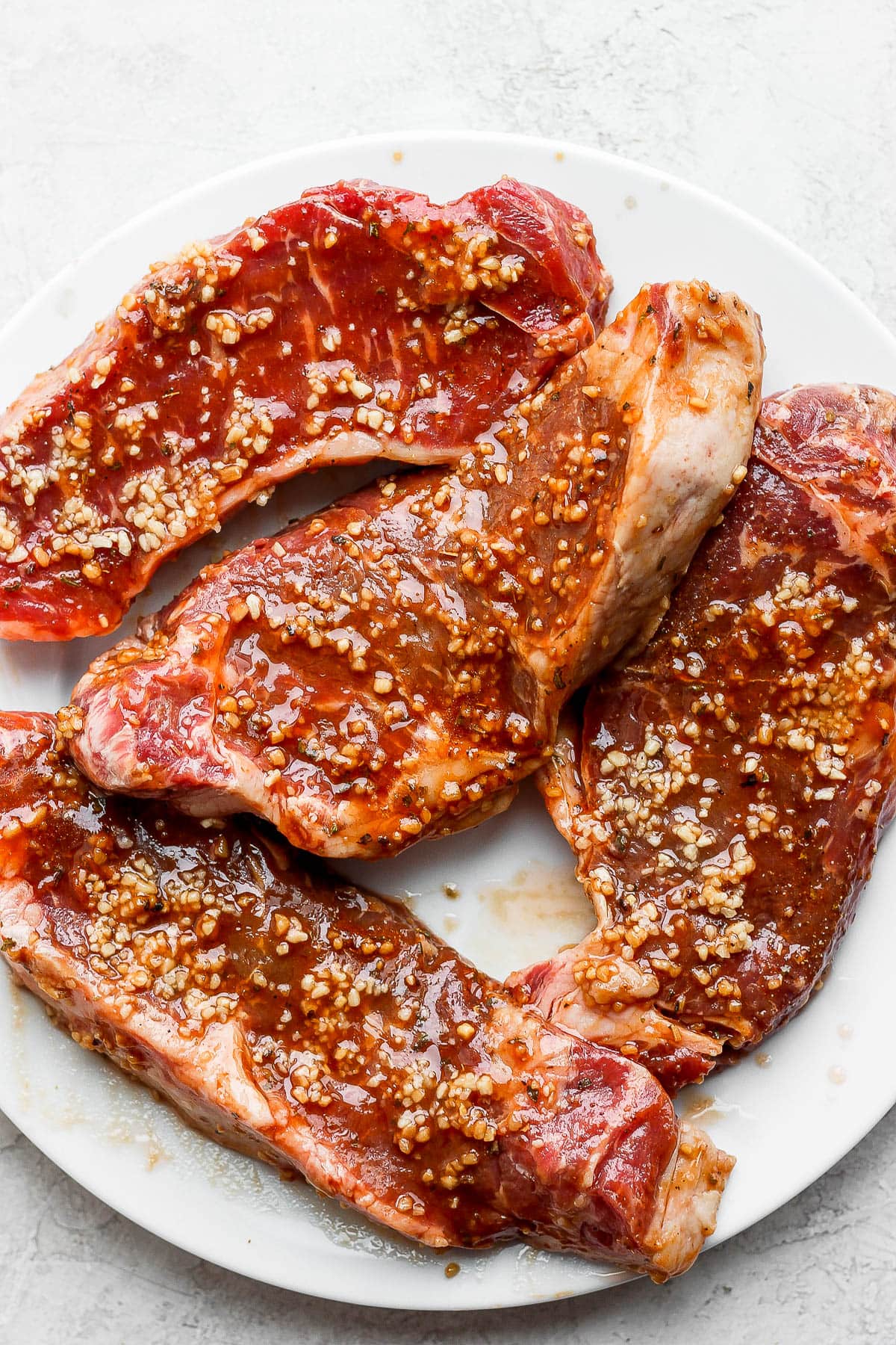 Four steaks on a plate covered in steak marinade. 