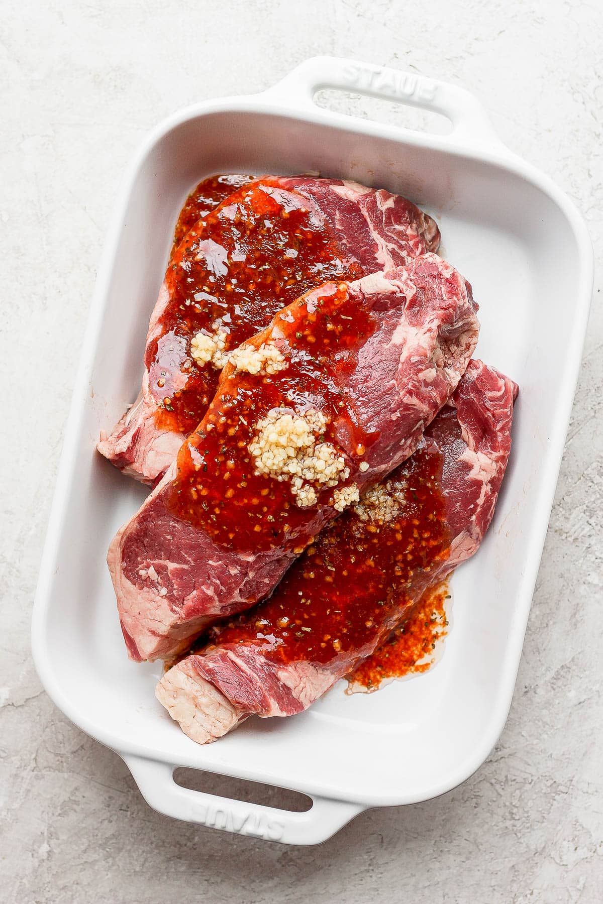 Three steaks in a white casserole pan with steak marinade on top. 