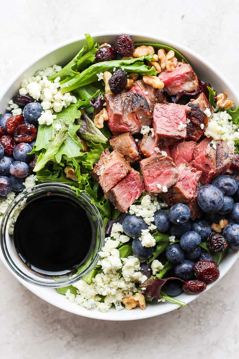 Easy steak salad in a bowl with a small dish of dressing.