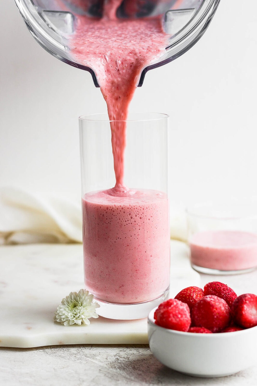 A strawberry banana smoothie being poured from a blender to a glass.