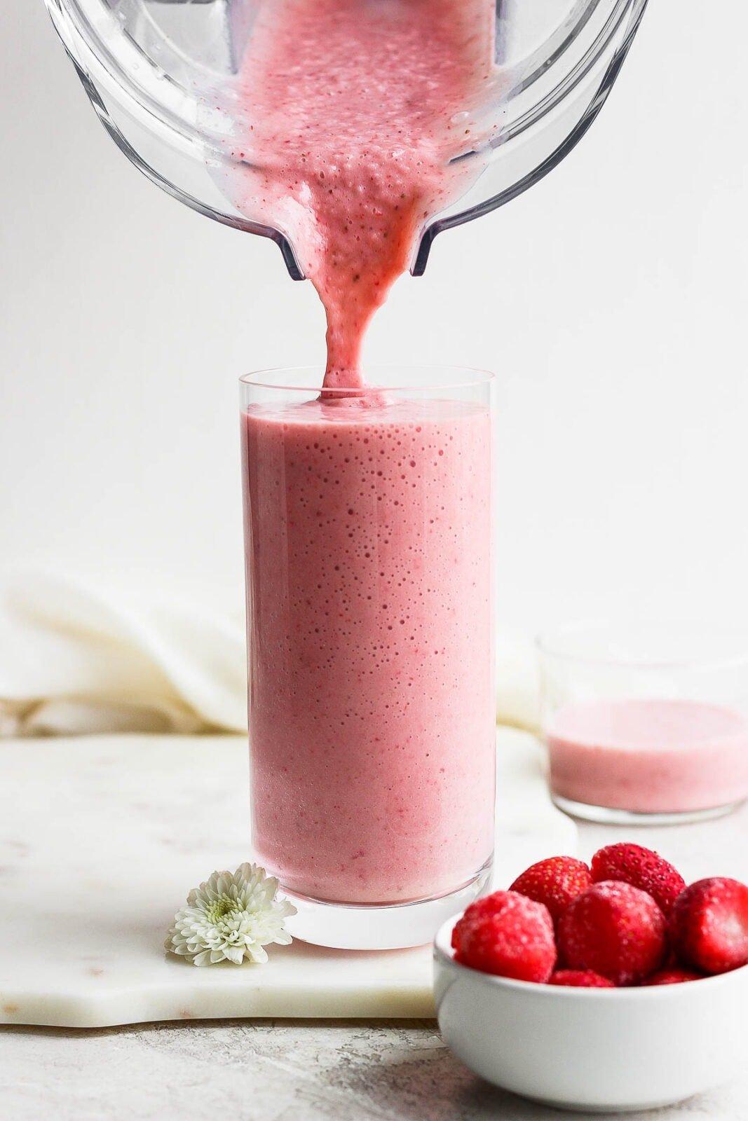 A strawberry banana smoothie being poured from a blender into a glass.