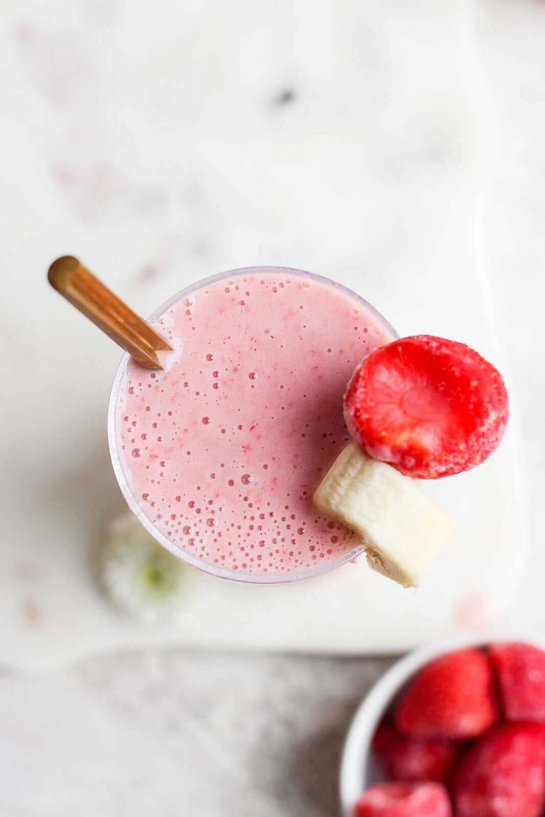 A strawberry banana smoothie in a glass with a spoon and a slice of strawberry and banana on the top.