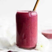A tall glass with a cherry smoothie and a straw sticking out of the top.
