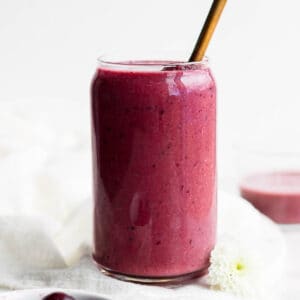 A tall glass with a cherry smoothie and a straw sticking out of the top.