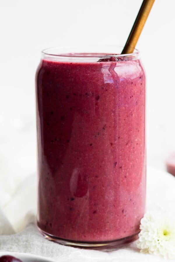 A tall glass with a cherry smoothie and a straw sticking out of the top.