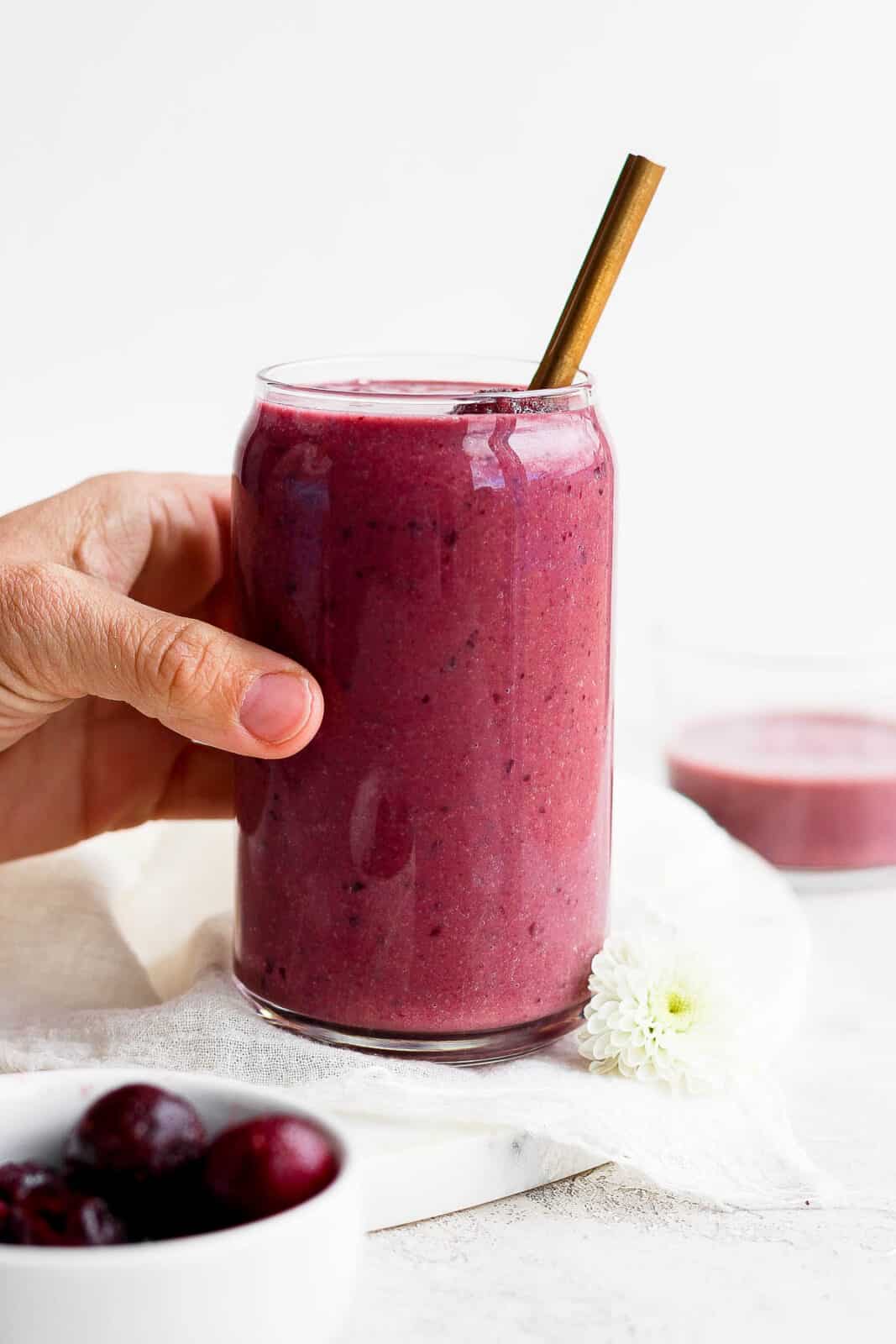 A hand grabbing a cherry smoothie.