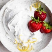A bowl of homemade dairy free whipped cream with strawberries and lemon zest.