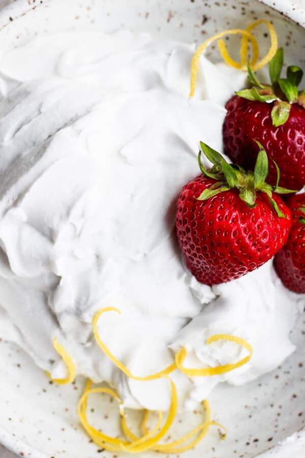 A bowl of homemade dairy free whipped cream with strawberries and lemon zest.