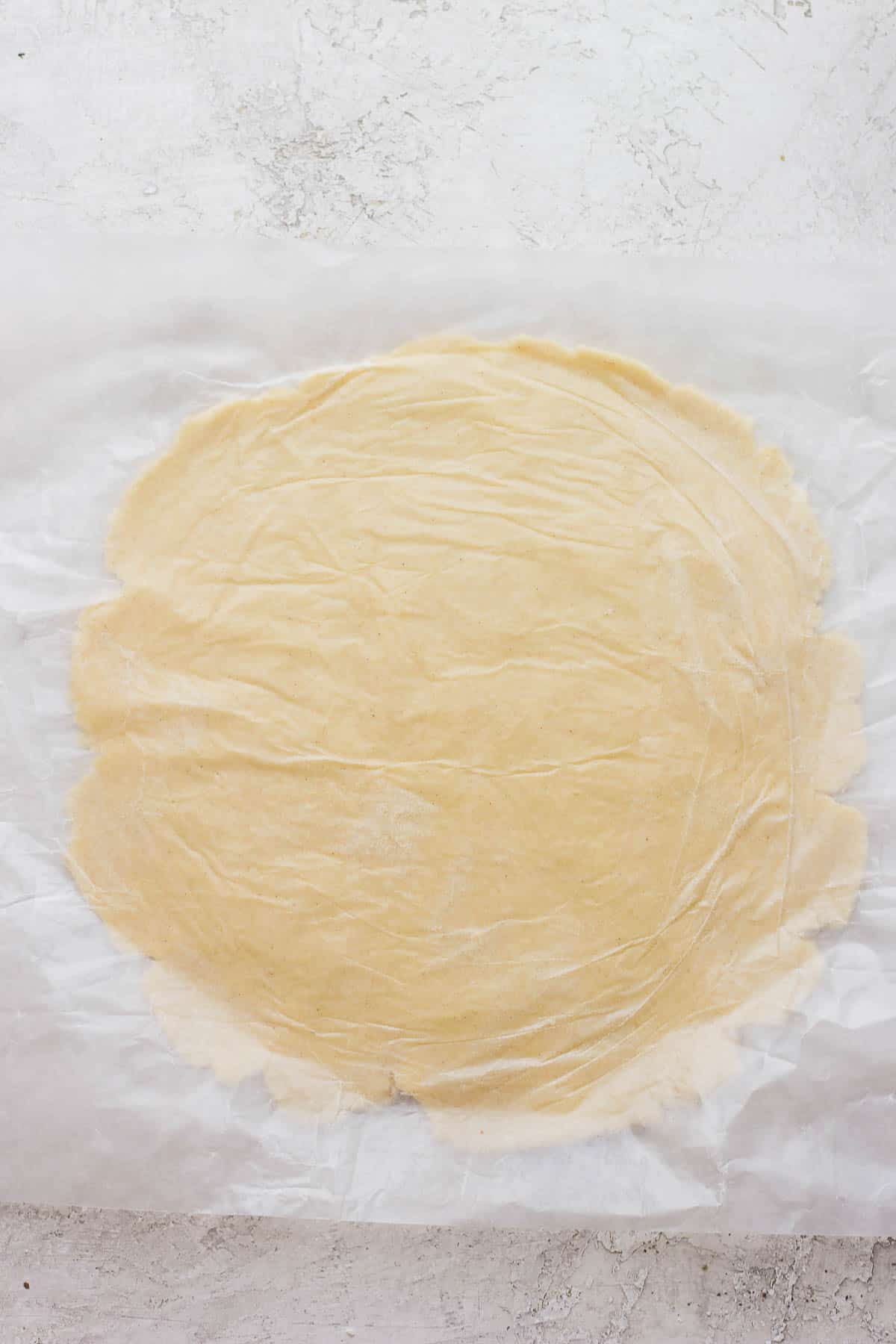 Dough rolled out into a large circle between two pieces of wax paper.