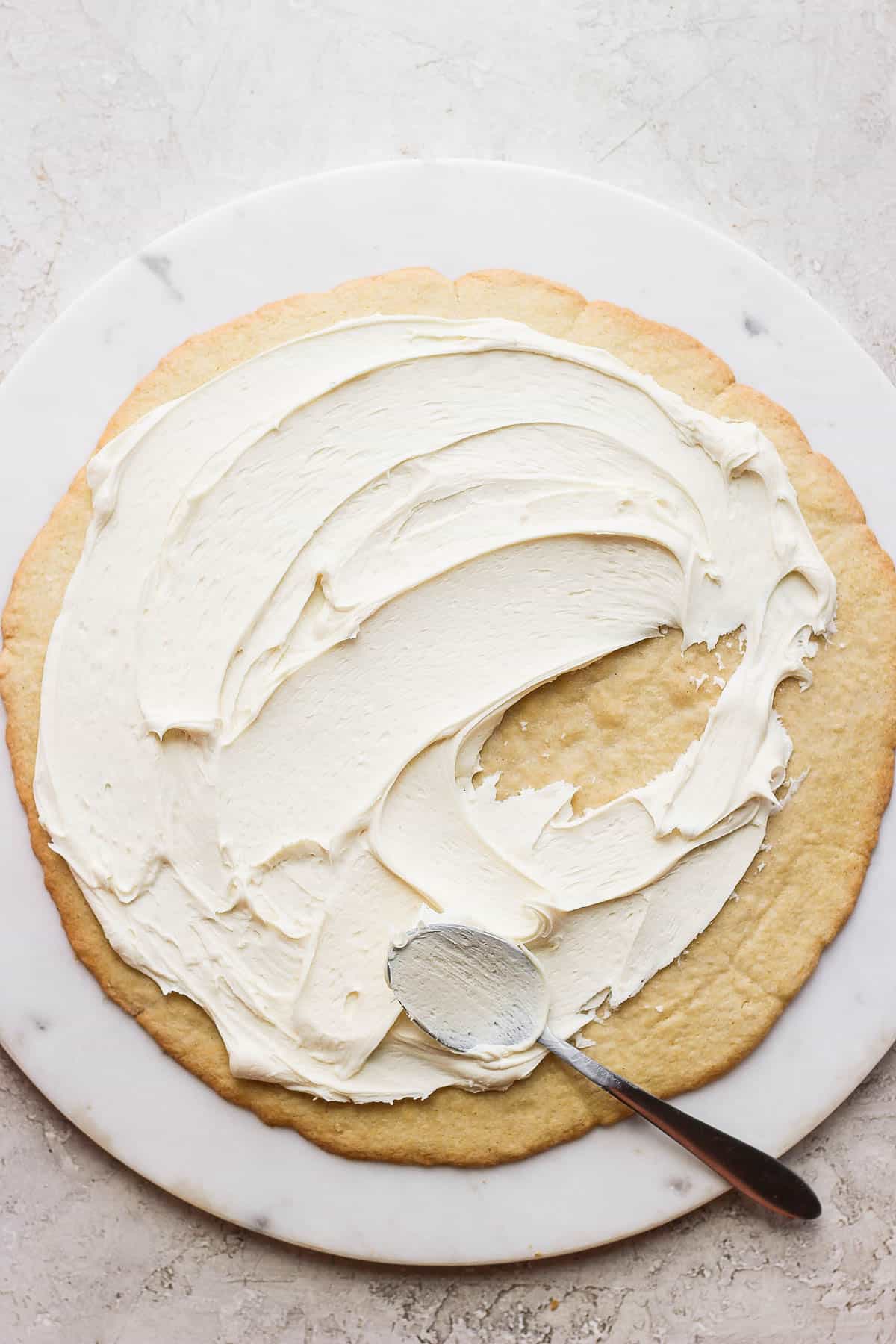 A large sugar cookie on a marble board with cream cheese frosting on top. 