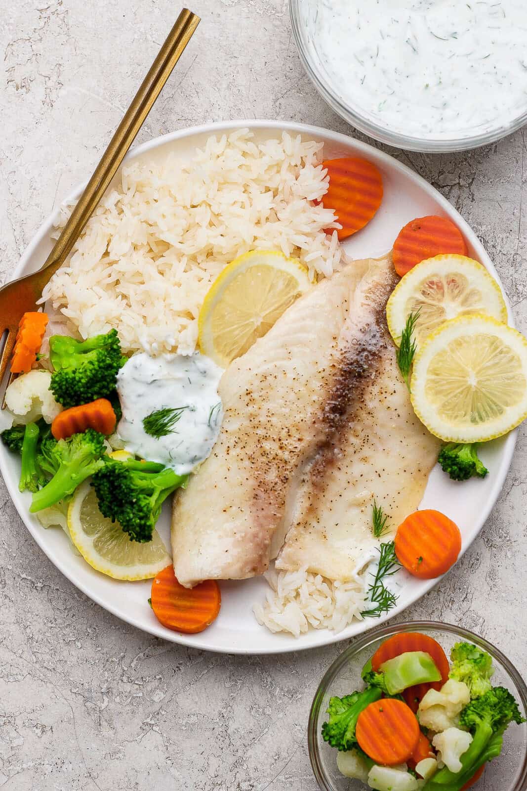 A plate with a baked tilapia filet, roasted veggies, white rice and tartar sauce with a fork sticking out.