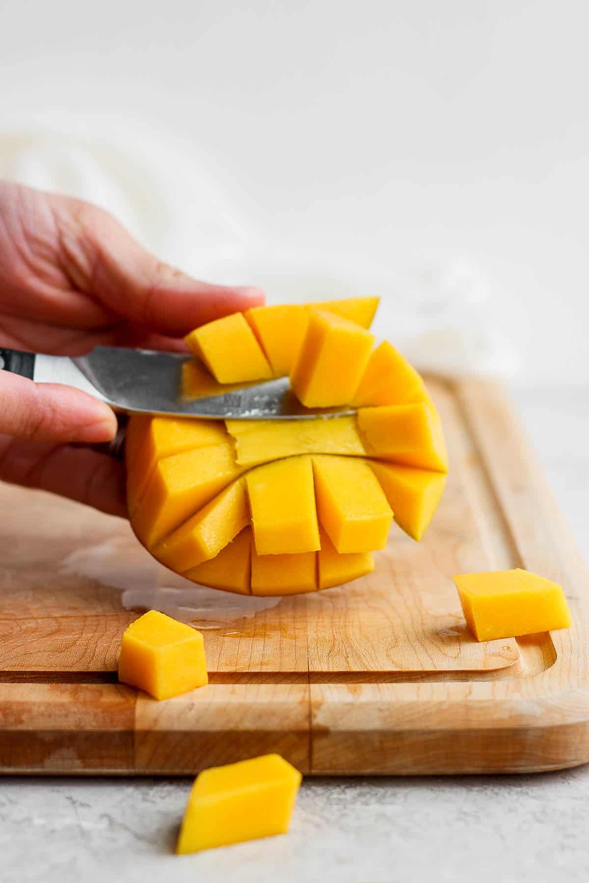 The cubes of mango being sliced from the skin.