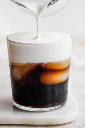 Someone pouring homemade cold foam on top of iced coffee.