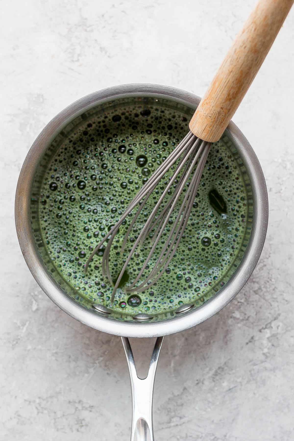 A small saucepan with matcha inside and a wooden whisk sticking out. 