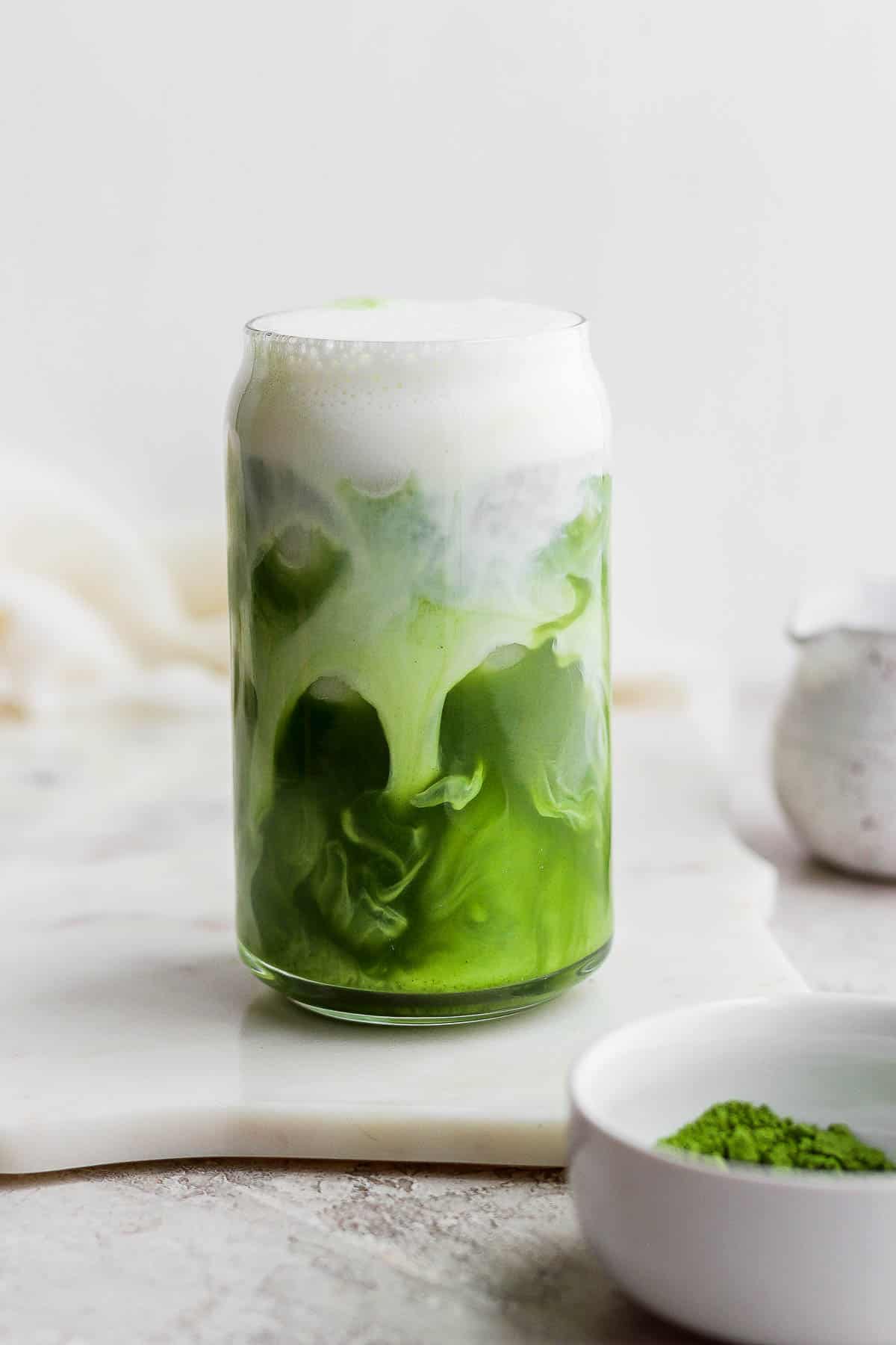 A glass of iced matcha latte with almond milk swirling inside. 