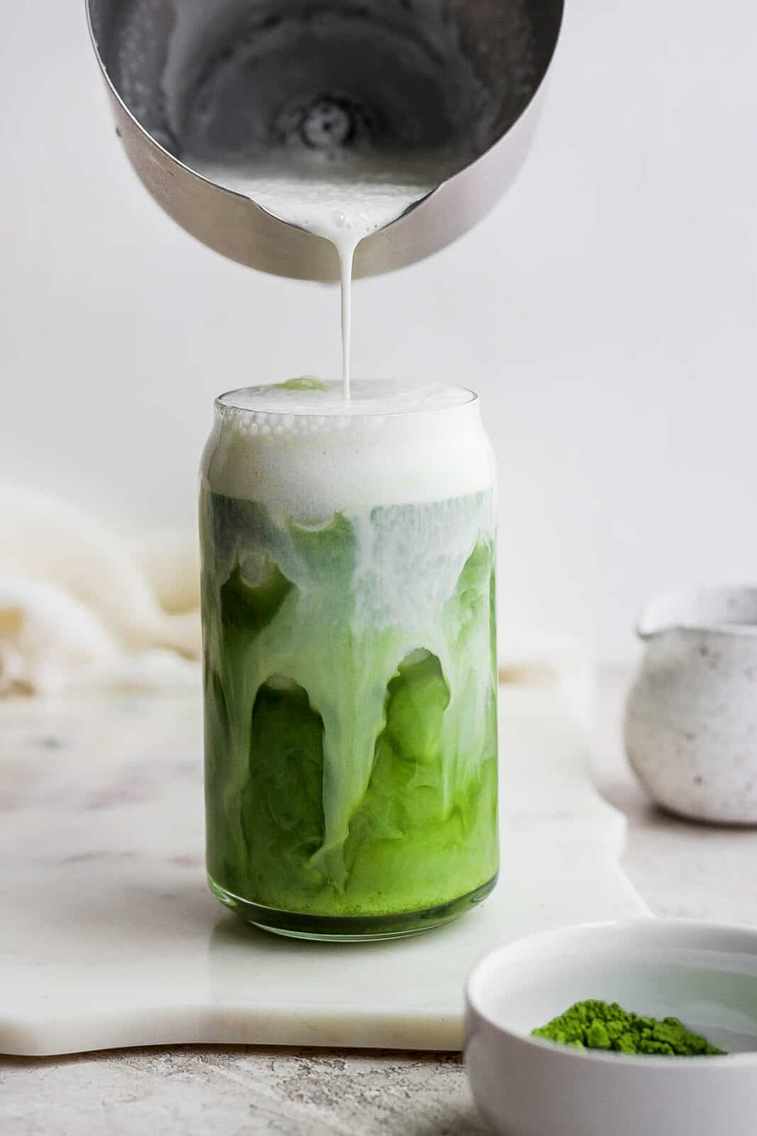 Someone pouring cold foam into a glass of matcha. 