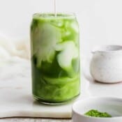 Someone pouring almond milk into an iced matcha latte.