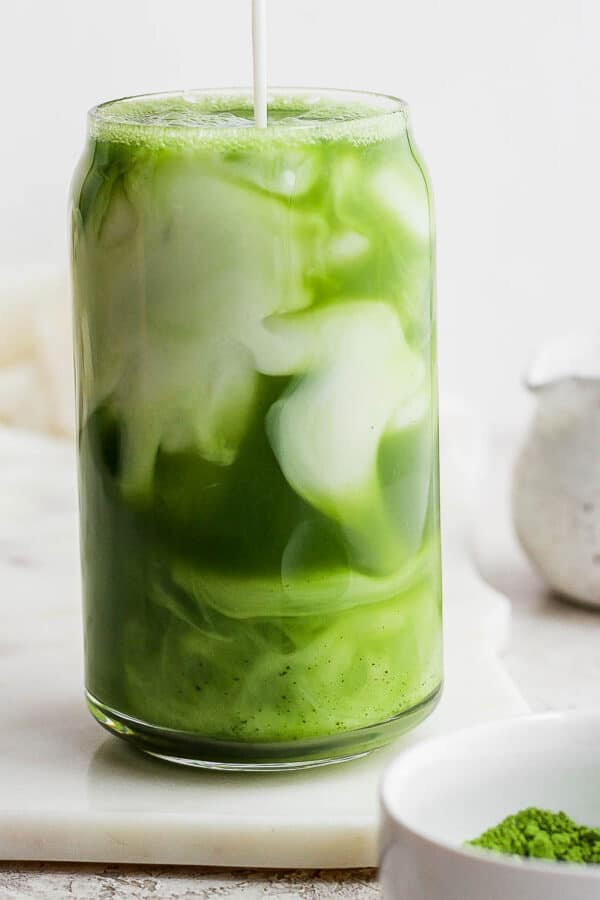 Someone pouring almond milk into an iced matcha latte.