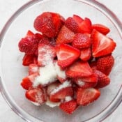 A large glass bowl with sliced strawberries and granulated sugar.