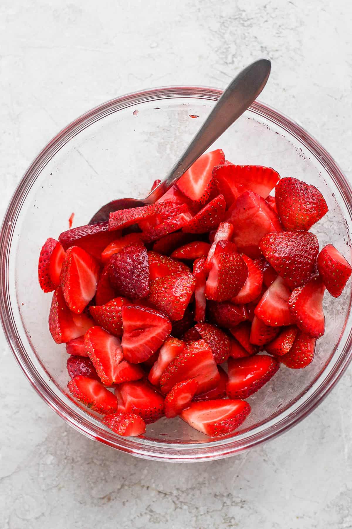 A glass bowl of macerated strawberries with a spoon.