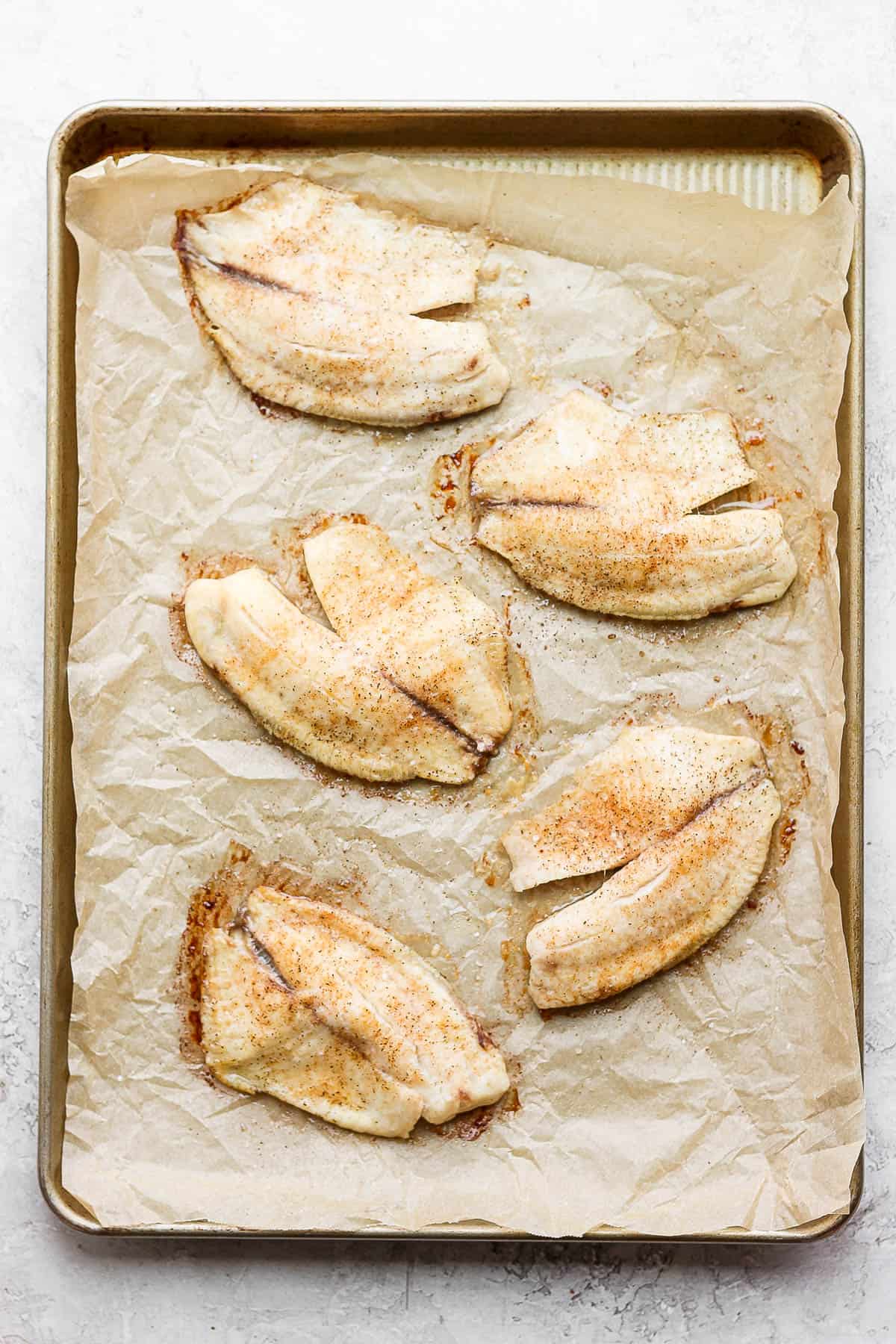 Baked tilapia fillets on a parchment-lined baking sheet.