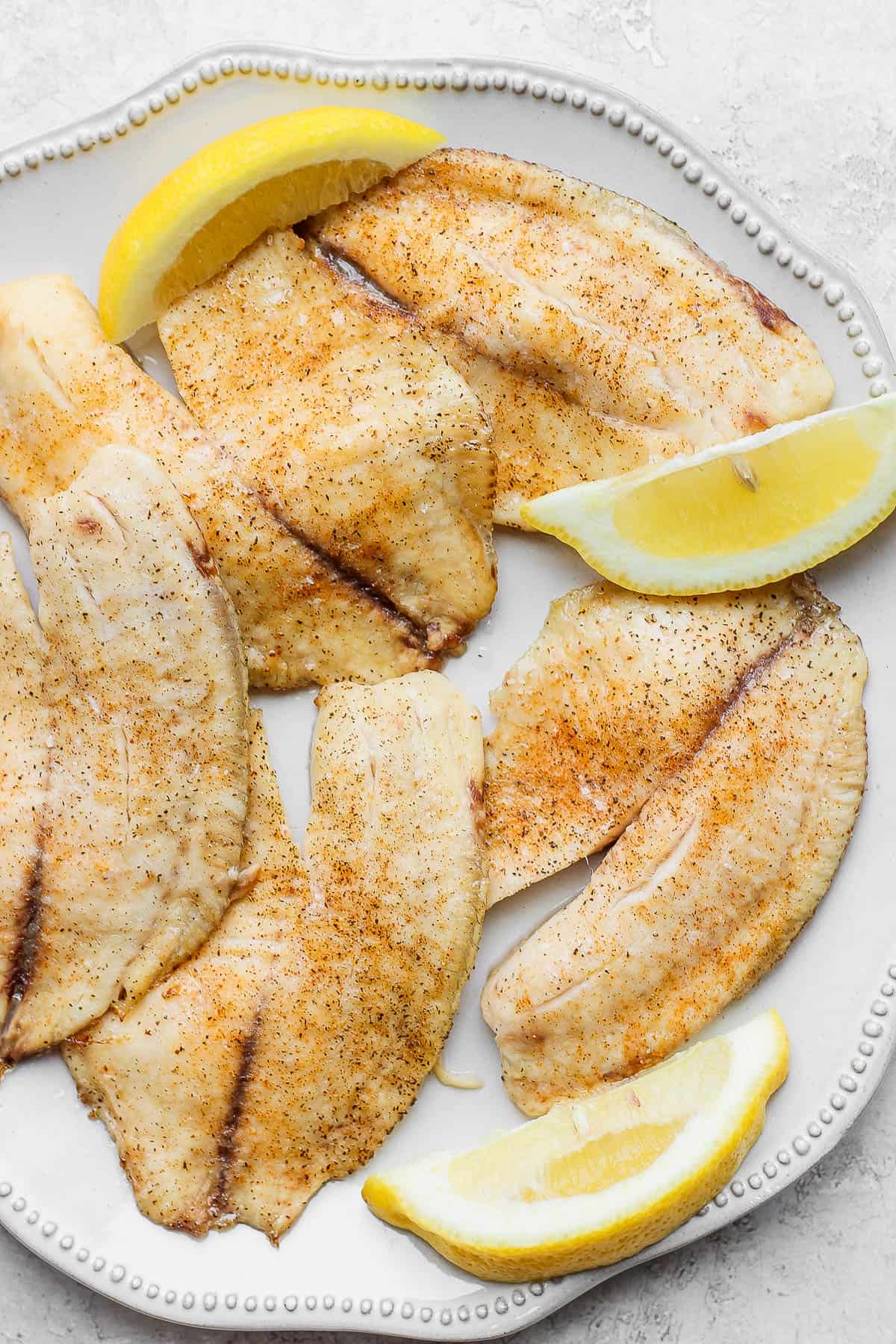 Baked tilapia fillets on a plate with lemon wedges.