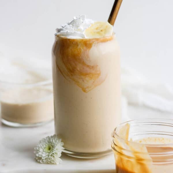 A peanut butter and banana smoothie in a glass with whipped cream and bananas on top.