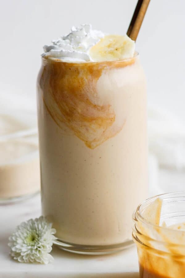 A peanut butter and banana smoothie in a glass with whipped cream and bananas on top.