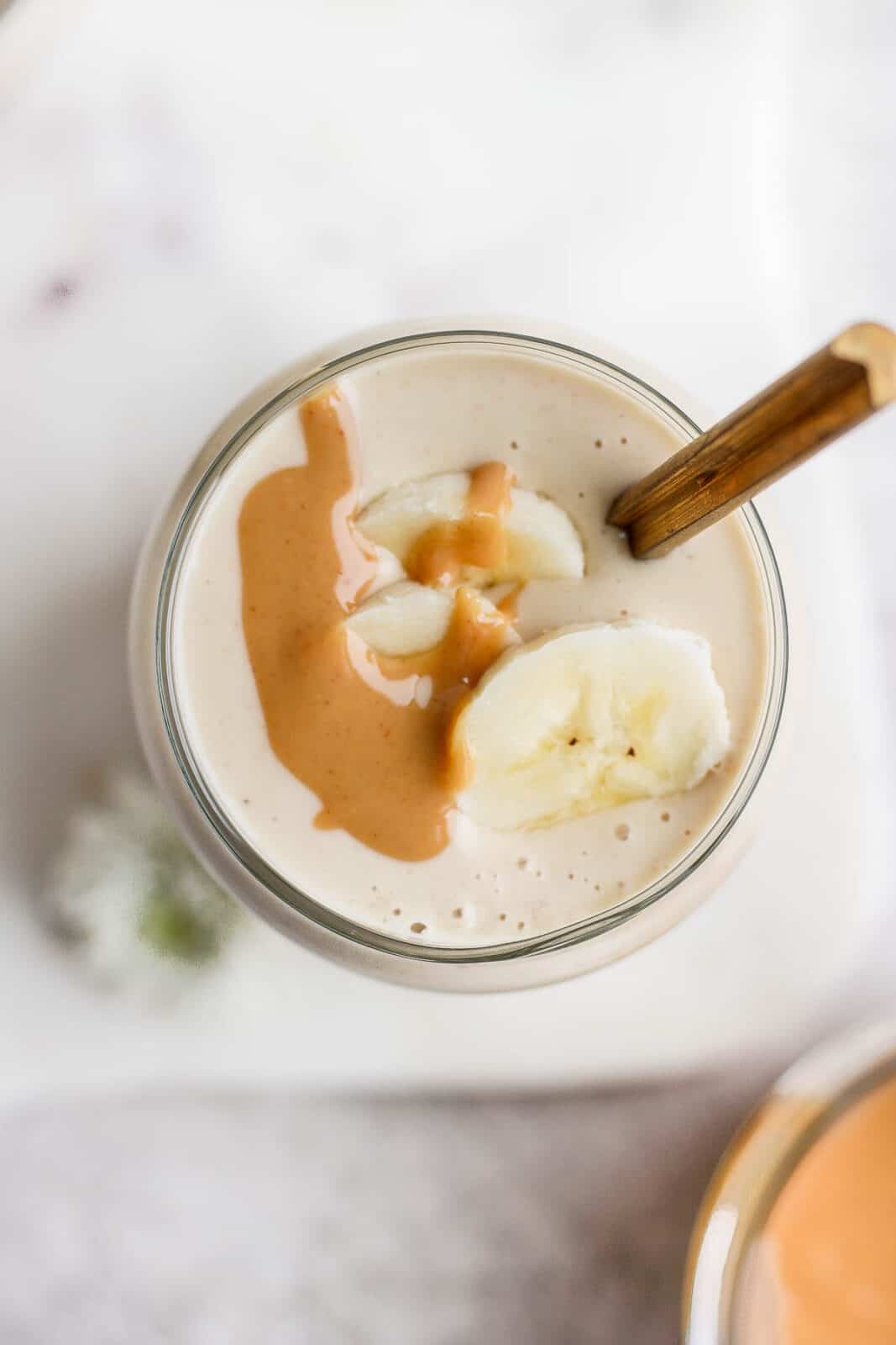 Peanut butter banana smoothie in a glass with some peanut butter and banana slices on top.